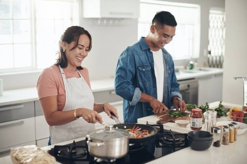 Couple smiling while cooking together in a bright modern kitchen.