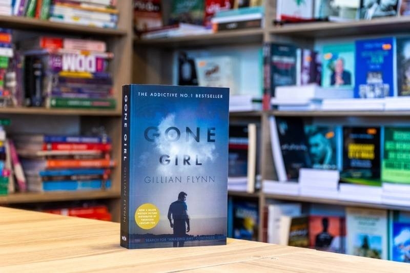 A copy of "Gone Girl" by Gillian Flynn displayed on a table in a bookstore with shelves of novels blurred in the background.