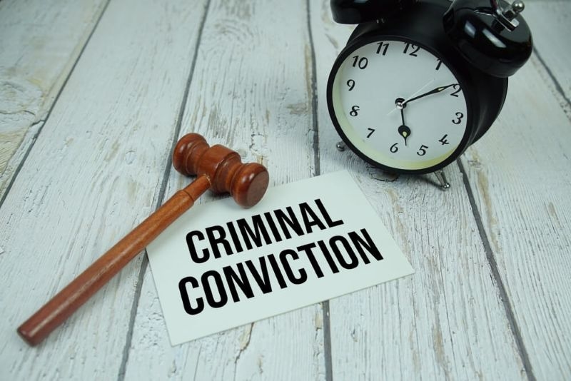 Criminal Conviction text on paper card with alarm clock and wooden judge gavel top view on wooden background