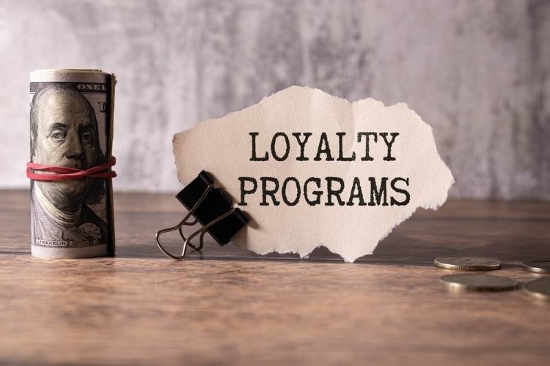 Rolled dollar bill and note labeled loyalty programs on a wooden table.