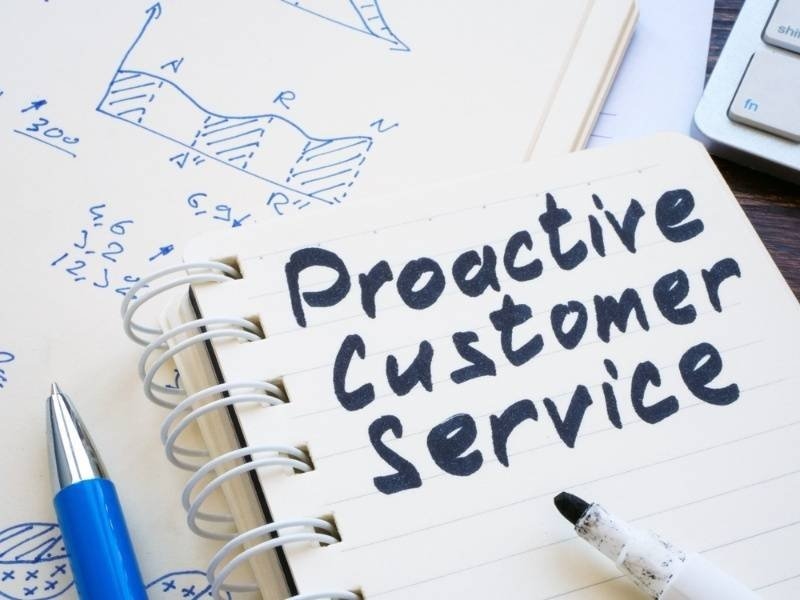 A notebook on a desk displays the handwritten words “Proactive Customer Service,” accompanied by pens and business notes.