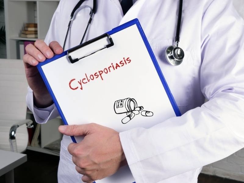 Doctor holding a clipboard labeled "Cyclosporiasis" with a medicine illustration.