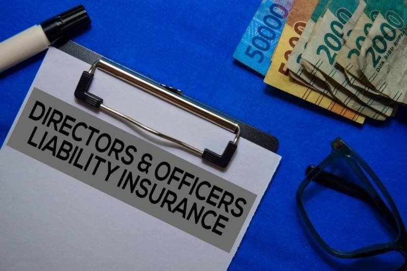 Clipboard labeled Directors & Officers Liability Insurance beside eyeglasses, currency notes, and office accessories.