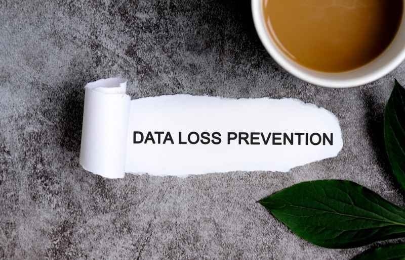 Paper displaying the words "Data Loss Prevention" on a desk beside a coffee cup and plant leaf.