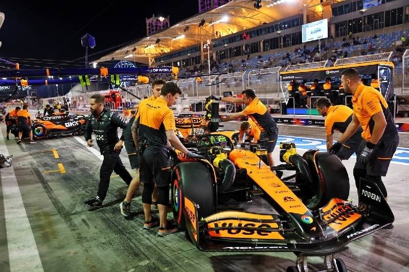 Formula 1 pit crew working around an orange McLaren race car during a pit stop at a nighttime circuit.