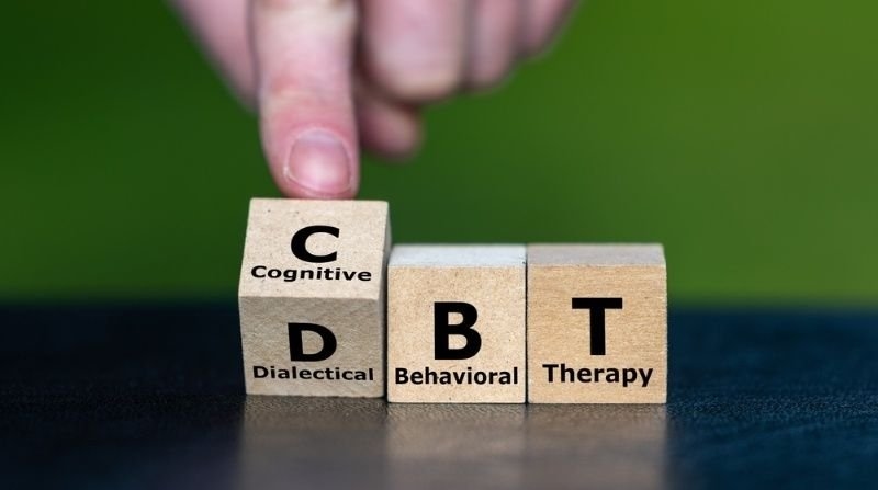 Hand arranging wooden blocks labeled Cognitive, Dialectical, Behavioral, and Therapy to illustrate DBT therapy concepts.