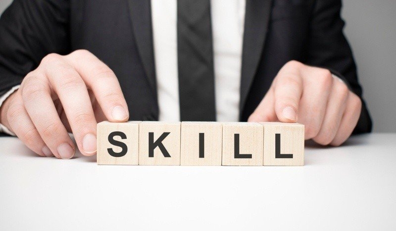 Business professional arranging wooden blocks spelling "SKILL."
