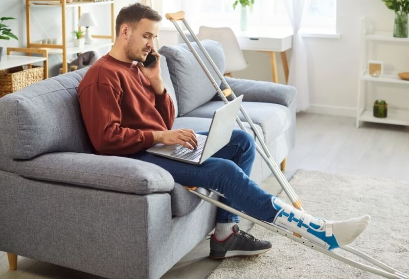 Disabled man talking on phone sitting on sofa with crutches on side