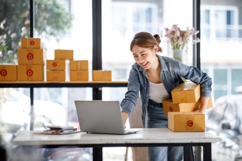Woman managing packages while working on a laptop, representing small business or online selling.