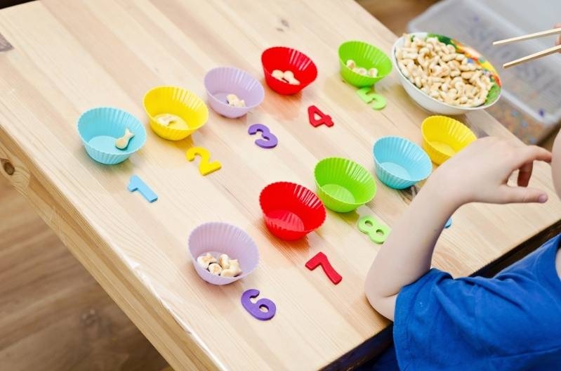 Child sorting snacks into colorful bowls with numbered labels on a table.