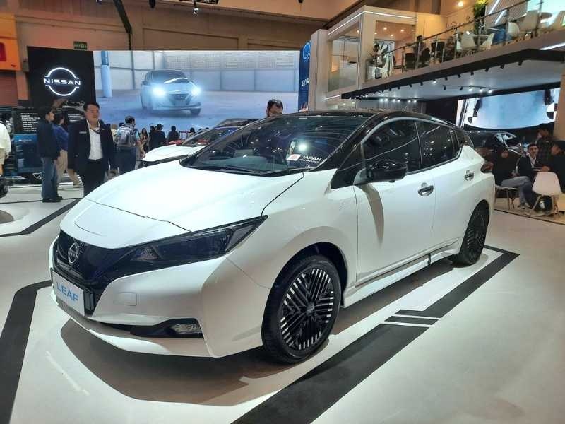 White electric car displayed at an auto show with people around, highlighting a modern EV showcase.