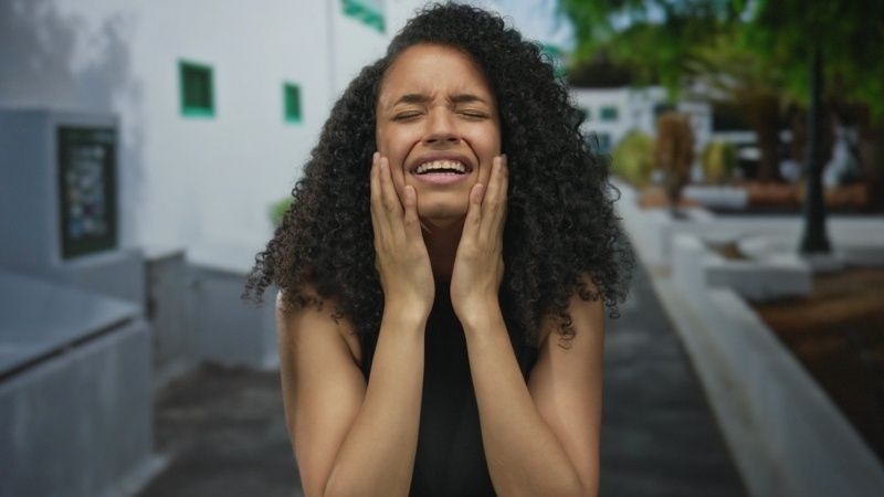 Woman outdoors holding her face and crying with an emotional expression.