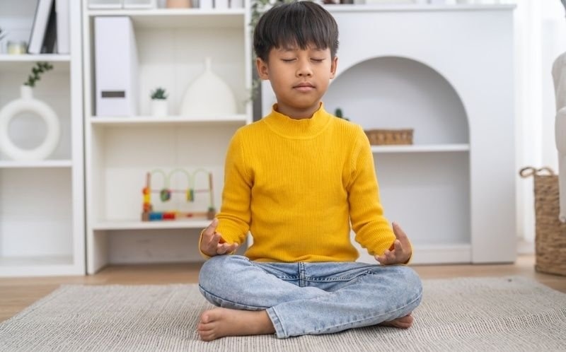 Asian little boy sitting cross legged with closed eyes doing yoga meditation.