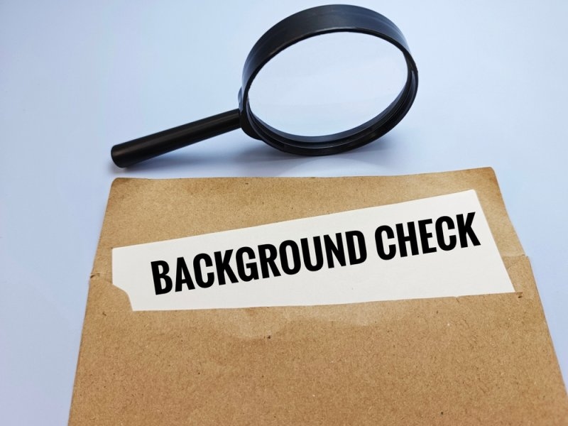 Envelope labeled “BACKGROUND CHECK” with a magnifying glass placed above it.