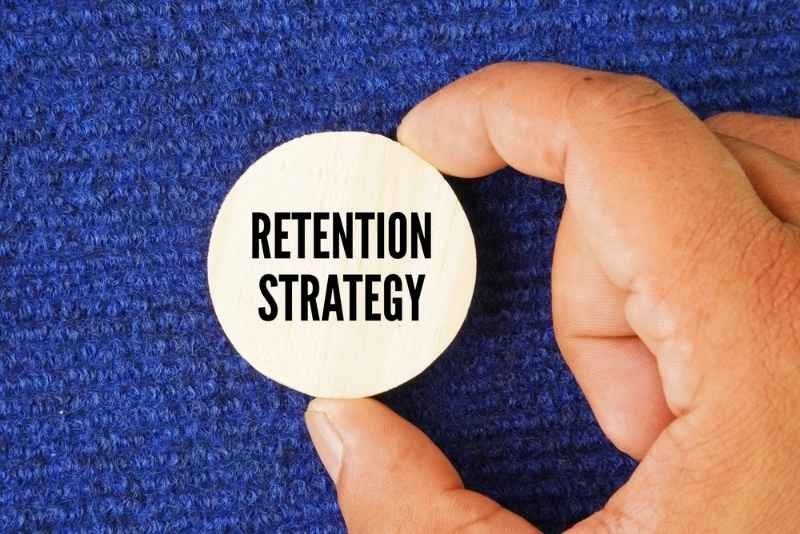 Hand holding a wooden circle with the word “Retention strategy.”
