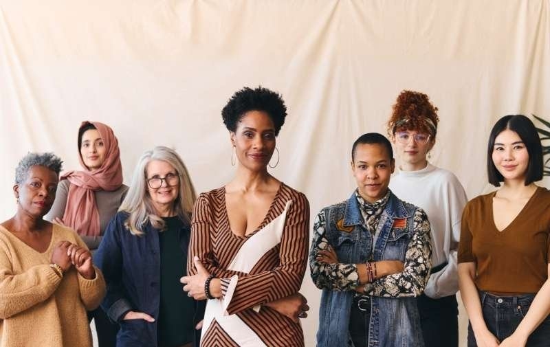 A diverse group of women of different ages and backgrounds standing together and smiling.