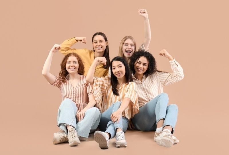 A diverse group of five young women sitting together and smiling while raising their fists.