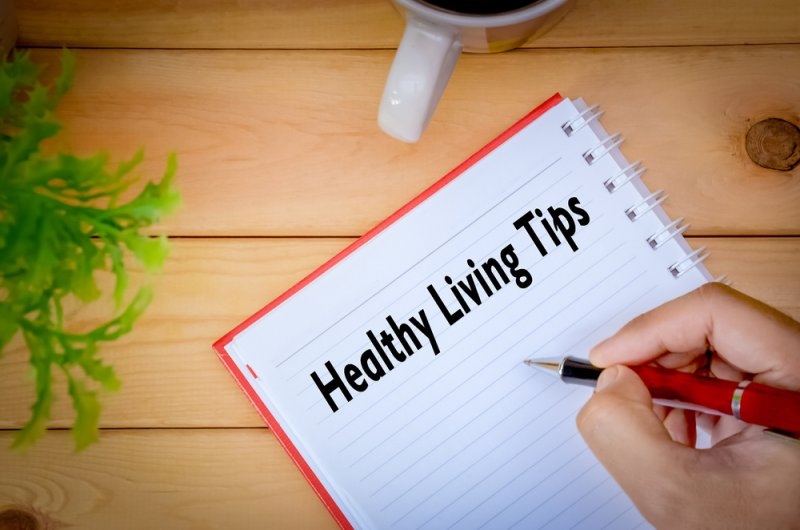 Hand writing “Healthy Living Tips” in a notebook on a wooden desk.