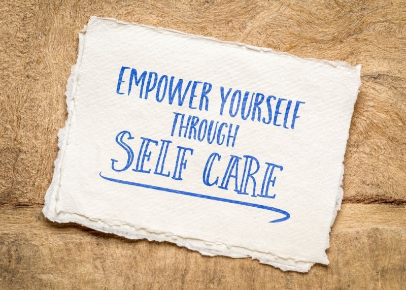 A handwritten message reading “Empower Yourself Through Self Care” on a sheet of textured paper.