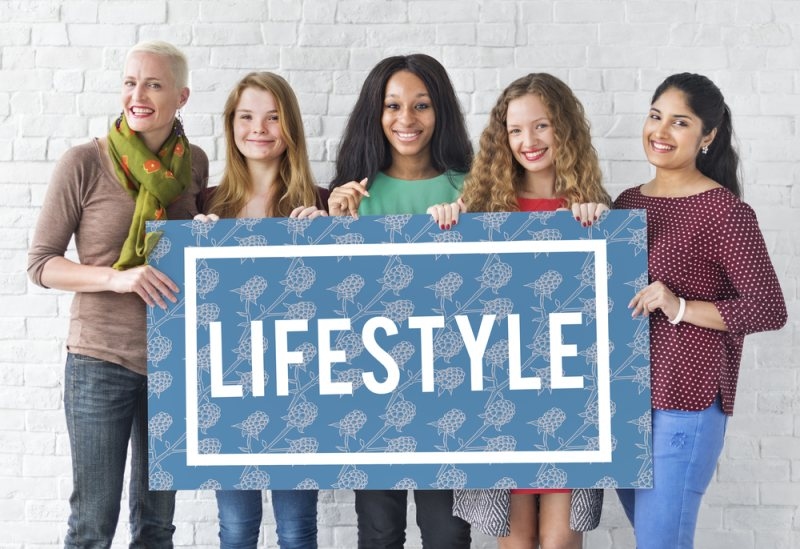 Five women holding a large sign labeled “LIFESTYLE,” representing women’s lifestyle, wellness, and empowerment.