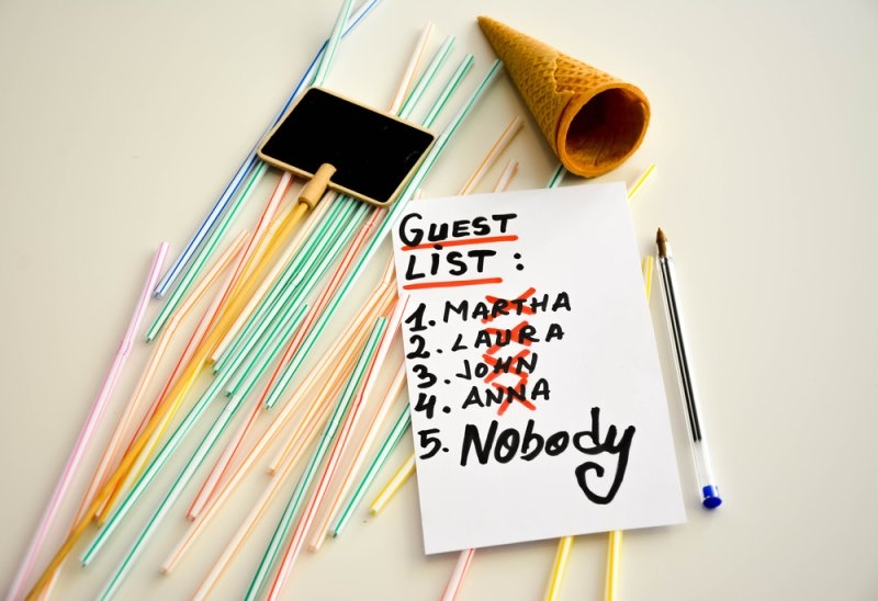 Overhead view of a handwritten guest list surrounded by colorful drinking straws, a chalkboard, an ice cream cone, and a pen.