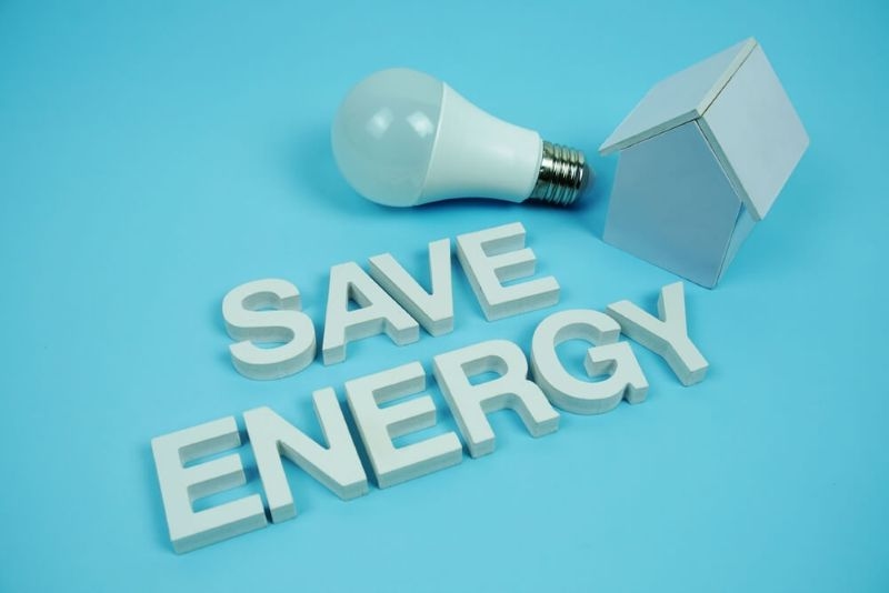 save energy text on blue background with bulb and a miniature house on side