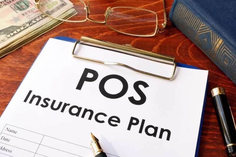 Clipboard displaying a POS insurance plan document alongside a pen, eyeglasses, cash, and a notebook.