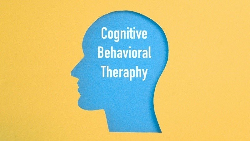 A blue silhouette of a human head appears against a yellow background, with the words “Cognitive Behavioral Therapy” displayed inside the head.