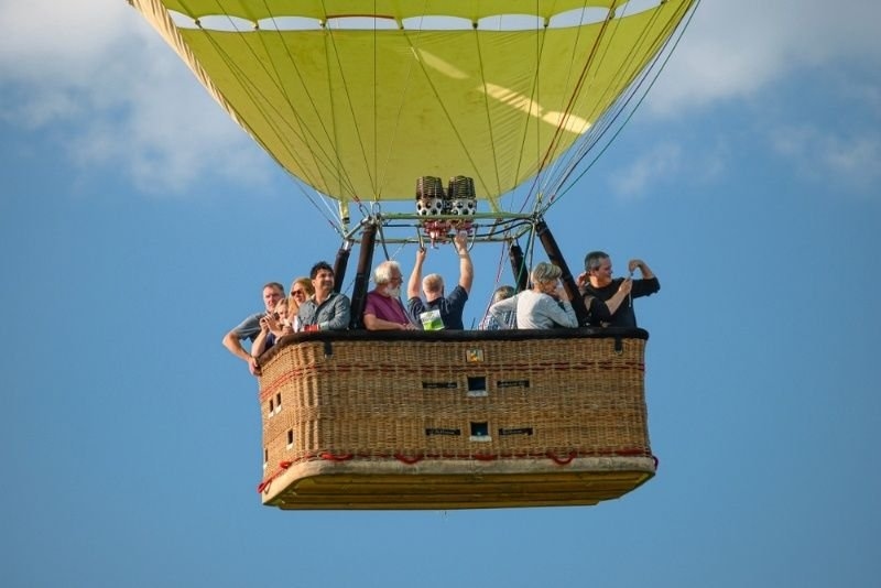 Passengers enjoying a scenic hot air balloon ride in a wicker basket against a clear blue sky.
