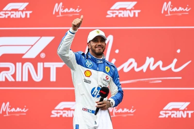 Formula 1 driver celebrating on stage with a thumbs-up gesture at the Miami Sprint event.