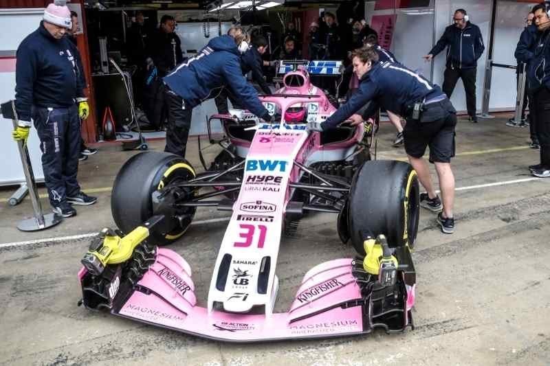 Formula 1 pit crew members push a pink race car in the pit lane during maintenance and race preparation.