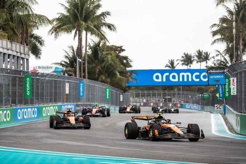 Several Formula 1 cars racing on a tropical street circuit lined with palm trees and Aramco advertisements.