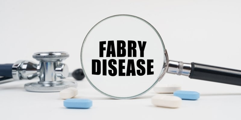 Stethoscope and assorted tablets arranged around a magnifying glass displaying the words “Fabry Disease” on a white background.