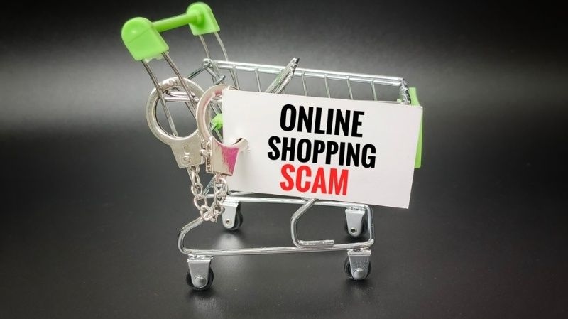 Mini shopping cart with sign reading online shopping scam on a dark background.