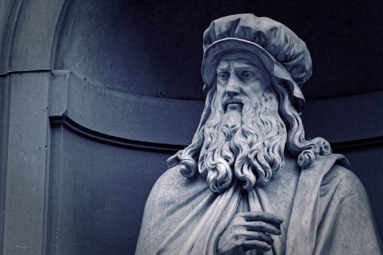 A detailed stone statue of a bearded Renaissance-era artist wearing a traditional cap and robes.
