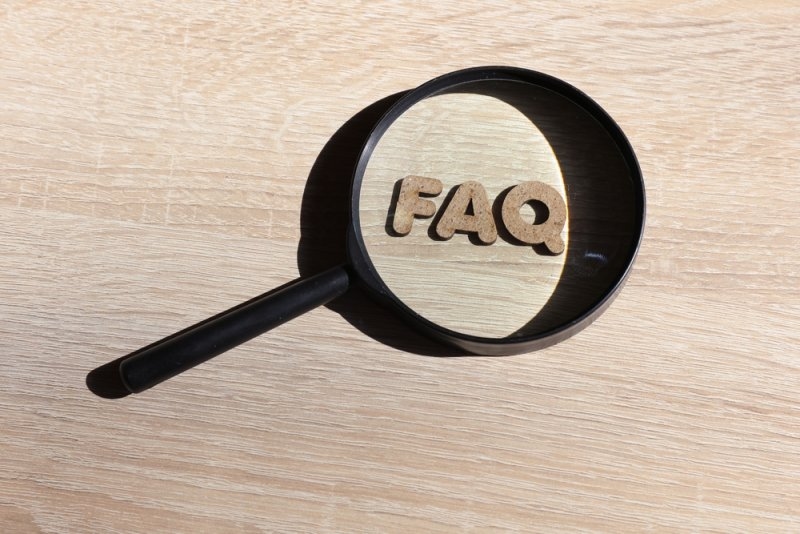 The word faq with wooden letters through a magnifying glass on a table.