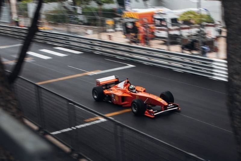 Red Formula racing car driving on a city street circuit during a high-speed race.