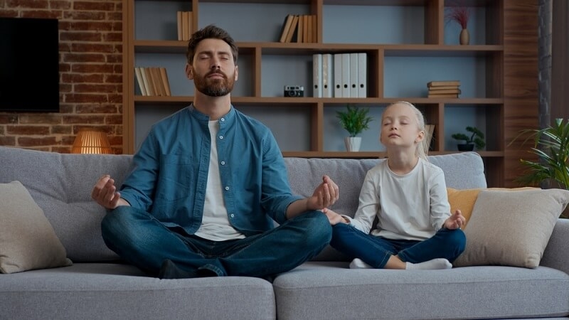 father and daughter doing meditation at sofa