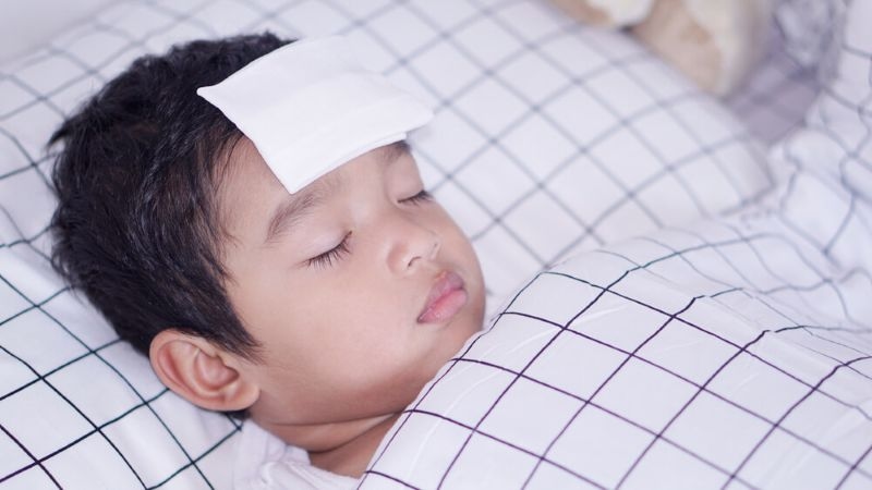 boy having high fever is resting with cooling pad on his head