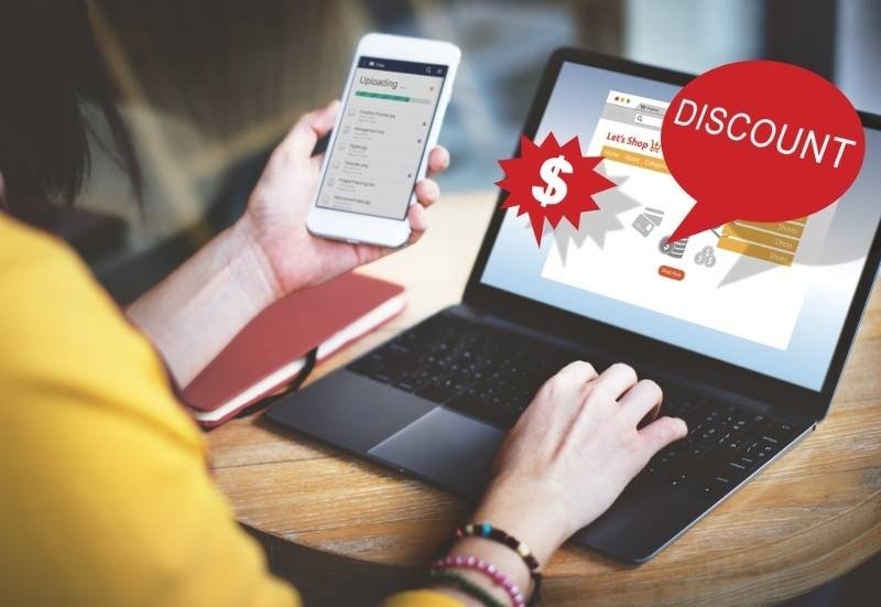 Person using a laptop and smartphone while browsing online deals, with discount graphics highlighting promotional offers, savings, and e-commerce shopping.