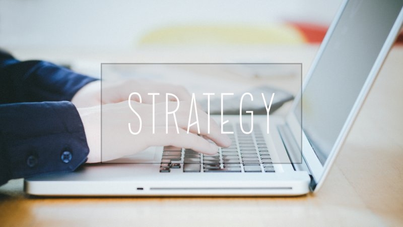 Strategy, text over young business man typing on laptop at desk in office environment.