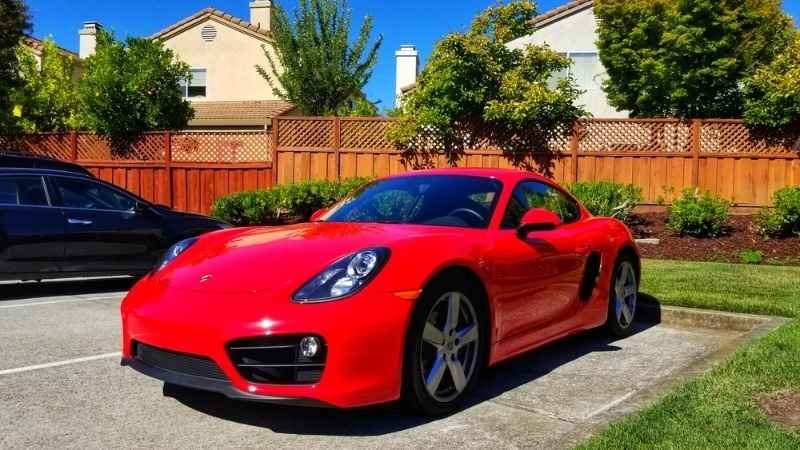 Red Porsche sports coupe parked in a residential parking area on a sunny day.