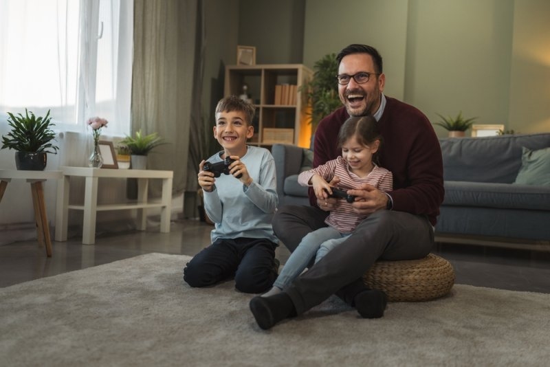Father and two children happily playing video games together at home.