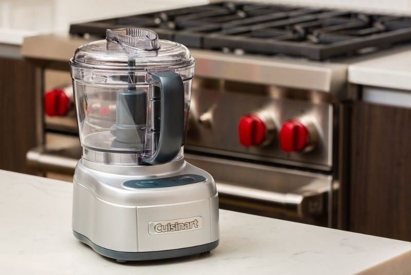 Compact food processor placed on a modern kitchen countertop with a stove in the background.