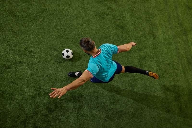 Overhead view of a soccer player kicking a ball on a grassy field.