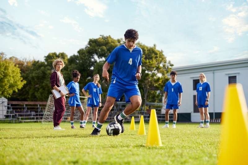 Youth soccer player dribbling a ball through cones during a training drill while teammates watch.
