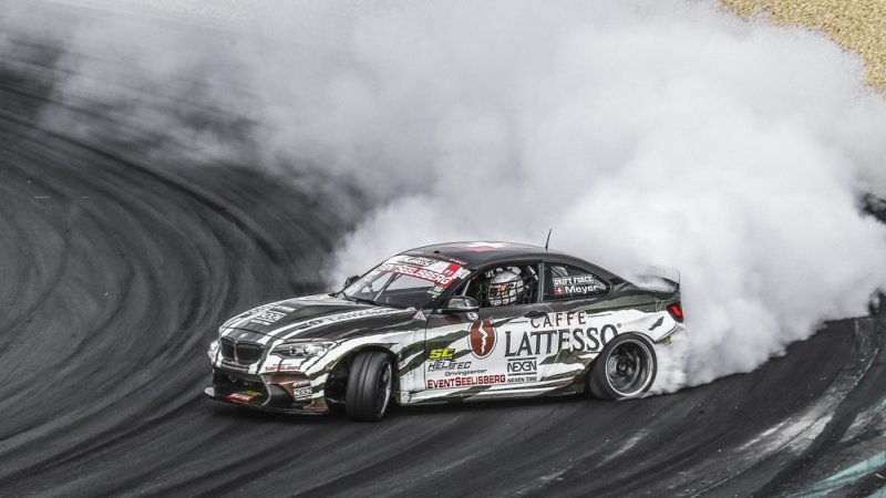 BMW race car drifting around a track, producing a large cloud of tire smoke.