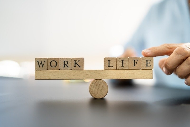 A wooden balance scale with “WORK” on one side and “LIFE” on the other, symbolizing work-life balance.