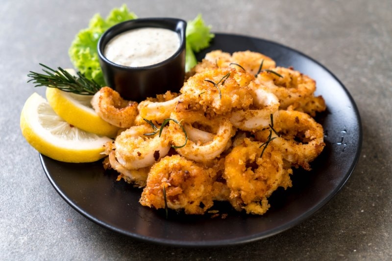 Plate of crispy fried calamari served with lemon wedges, herbs, and dipping sauce.