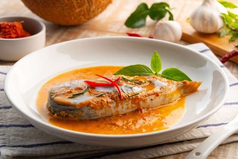Pan-seared catfish steak served in a rich creamy coconut curry sauce, garnished with basil leaves and red chili slices.